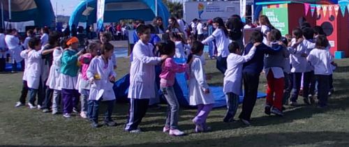 Chicos y chicas des escuale primaria, con guardapolvo blanco, jugando al aire libre. En color.