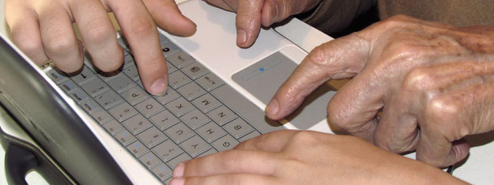 Manos de un abuelo y sus nietos sobre el teclado de una netbook. En color.